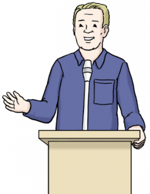 Auf dem Bild sieht man einen Mann. Er steht hinter einem Rednerpult mit Mikrophon und hält gerade eine Rede.